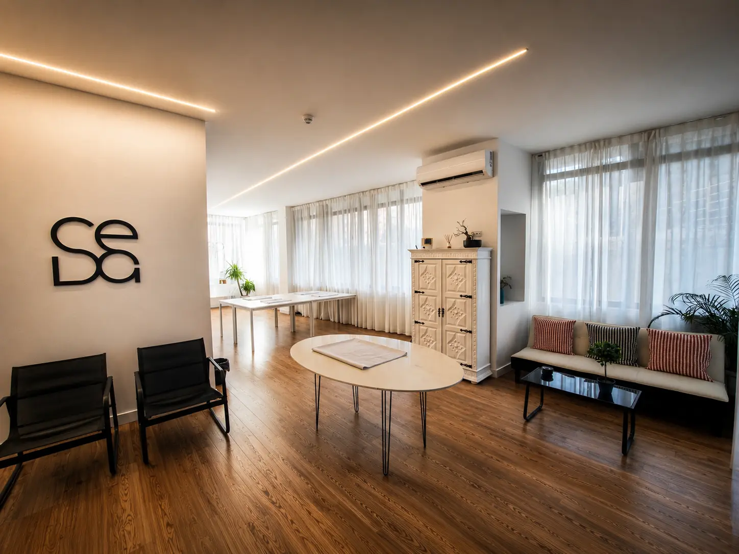 Sala da Seda Eventos com o logótipo na parede, sofá, cadeiras e grandes janelas com cortinados