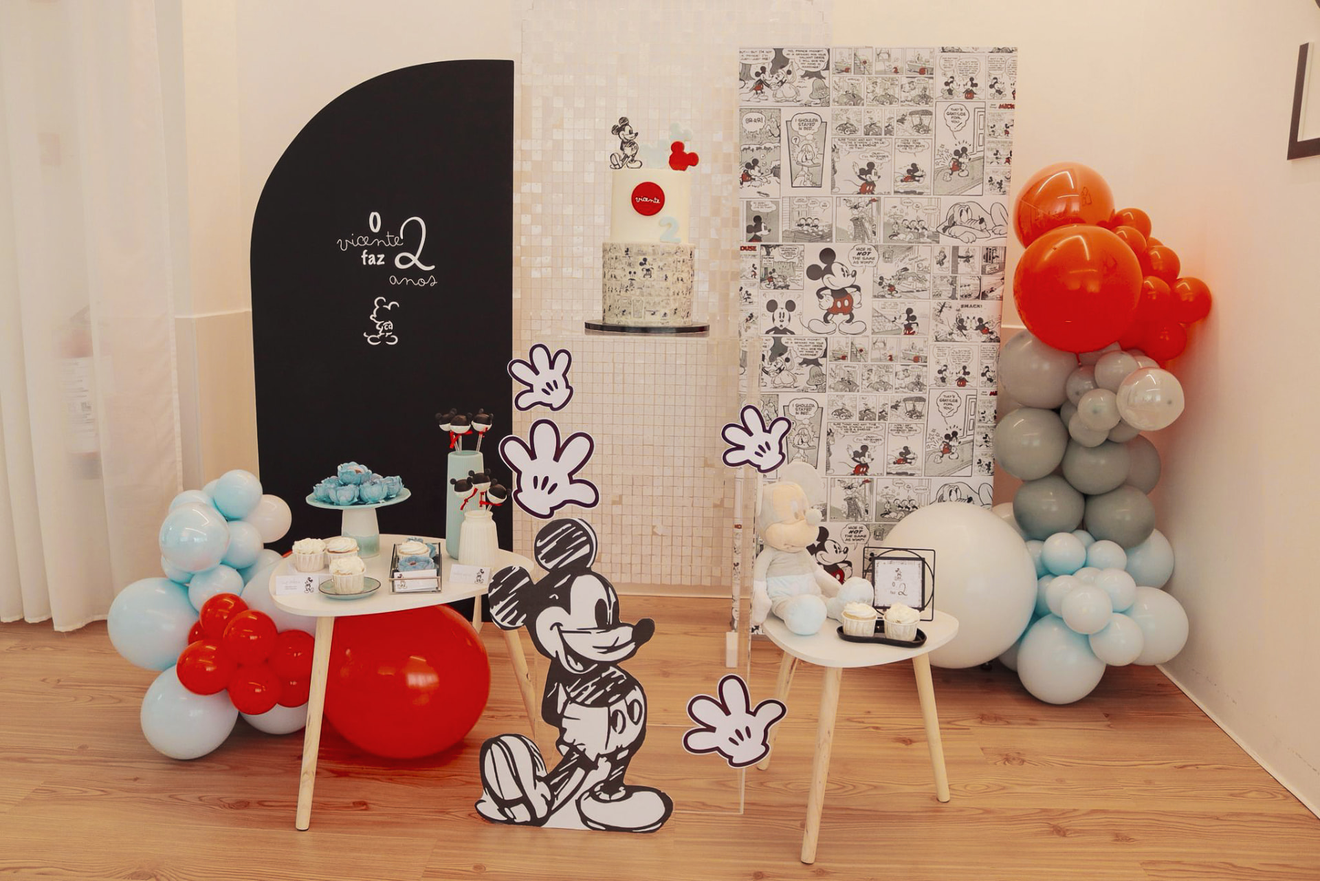 Decoração infantil com tema Mickey, balões vermelhos e cinzentos e mesa de doces